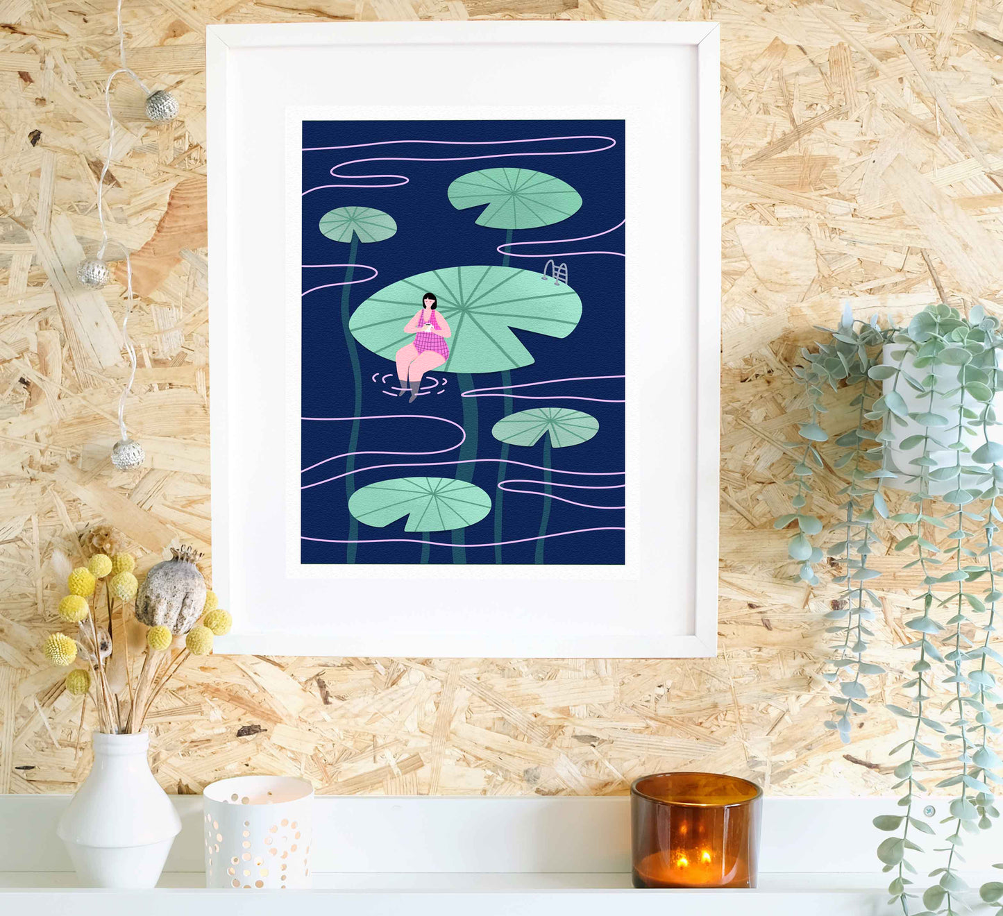 Framed artwork of a woman in a pink dress among lily pads on a blue background, displayed on a wall with decorative elements.