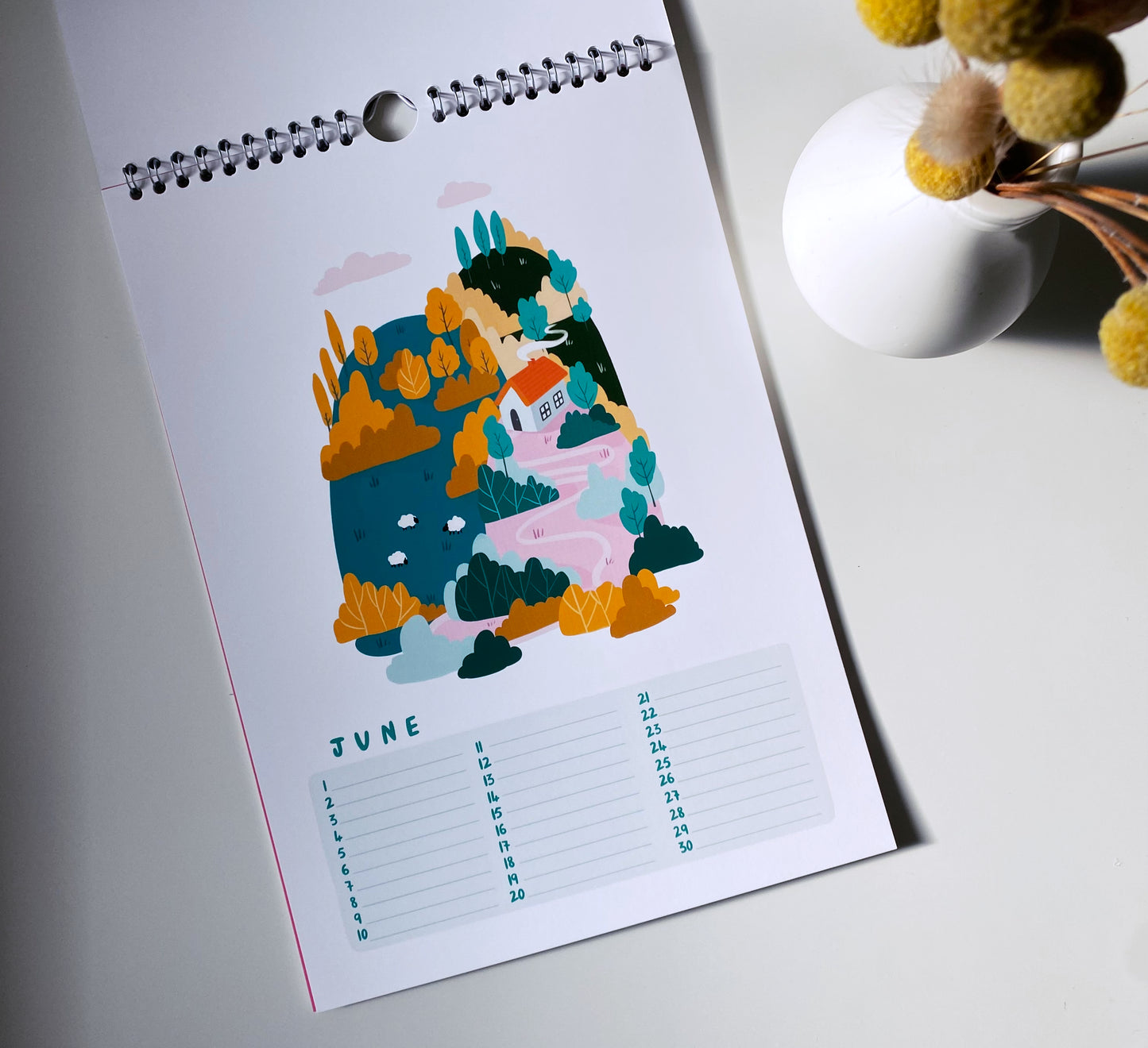 Calendar with a colorful illustration of a mountain and flowers on a white surface.