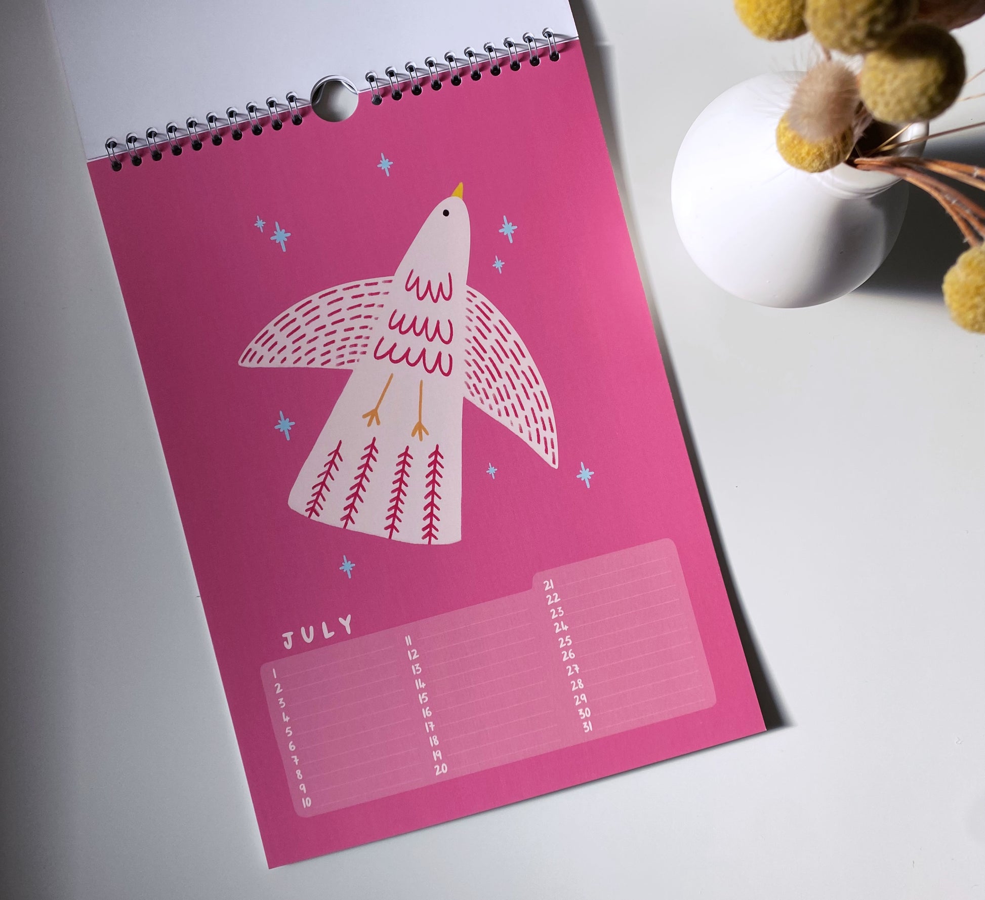 Pink calendar with a bird illustration on a white surface