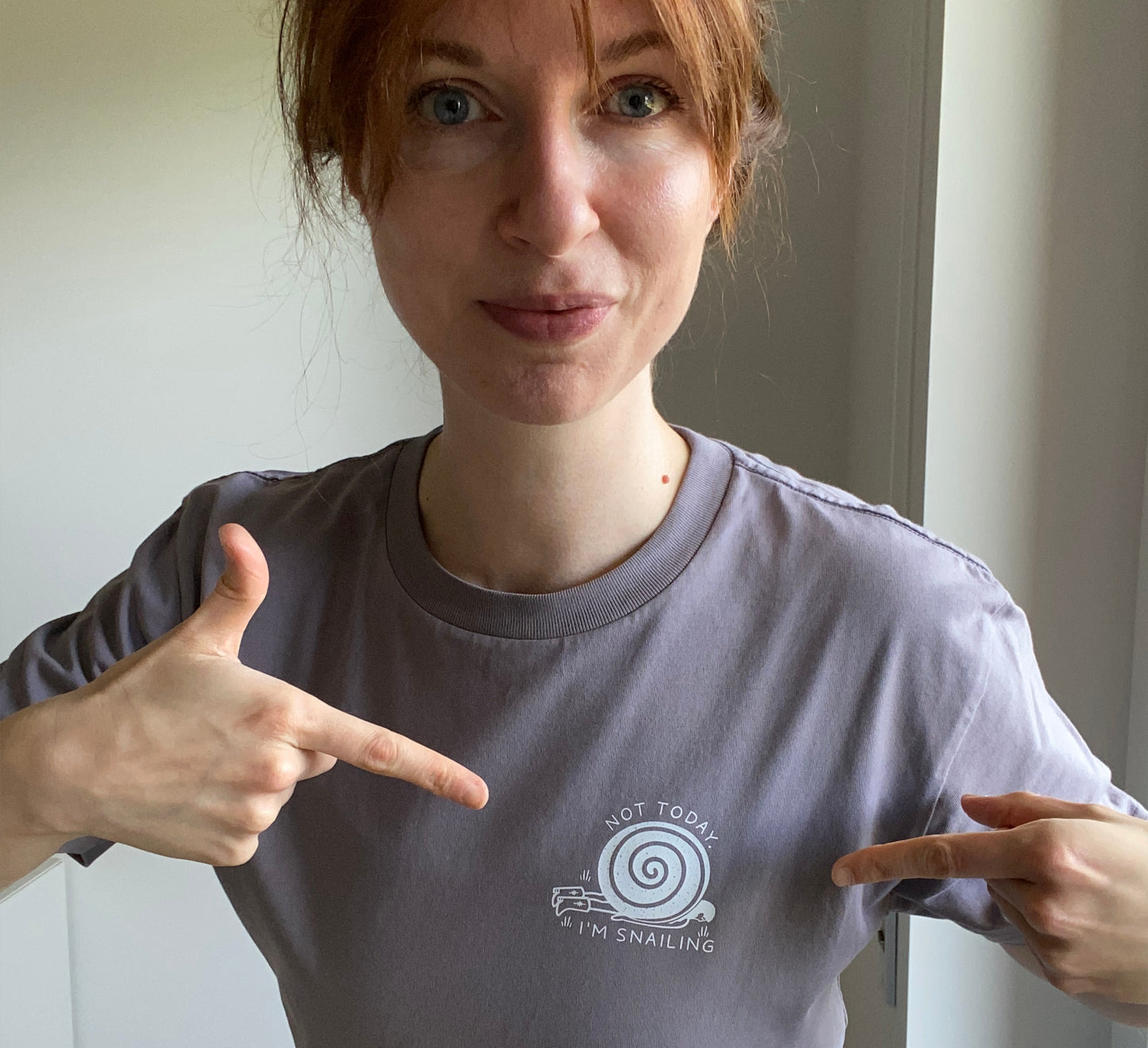 Person wearing an organic cotton gray t-shirt with a snail logo, standing against a neutral background